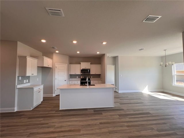 kitchen featuring dark hardwood / wood-style floors, appliances with stainless steel finishes, a kitchen island with sink, and white cabinetry