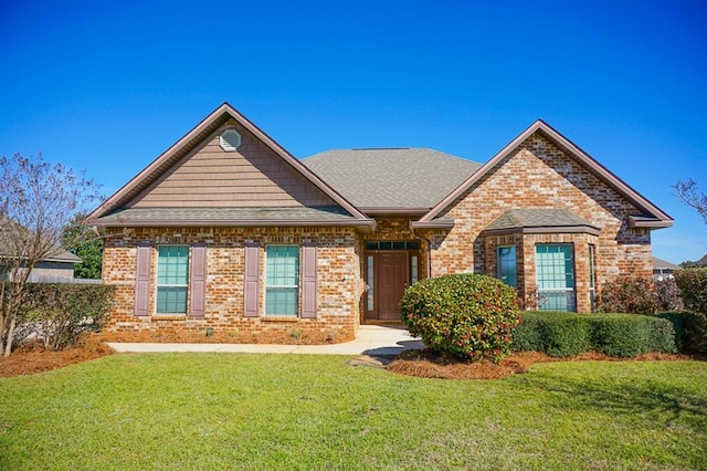 view of front facade featuring roof with shingles, a front yard, and brick siding