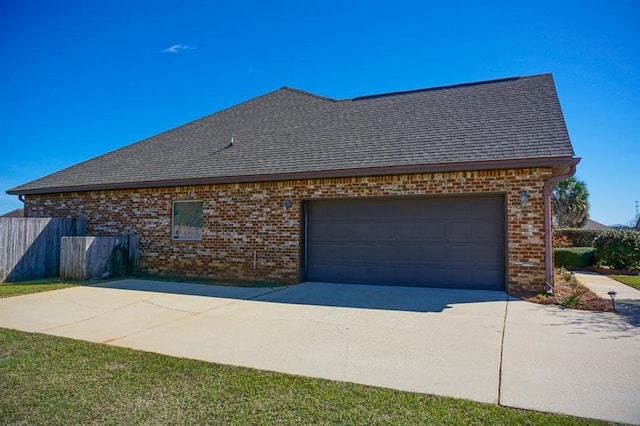 view of side of property with concrete driveway, brick siding, roof with shingles, and an attached garage