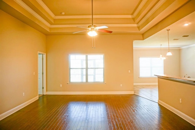 unfurnished room featuring ornamental molding, a tray ceiling, dark wood finished floors, and baseboards