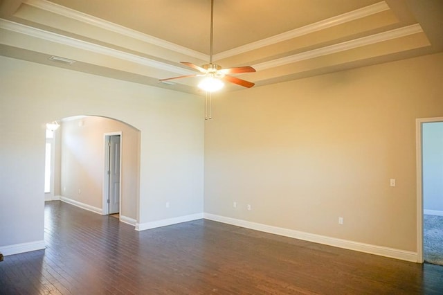 spare room featuring arched walkways, a raised ceiling, dark wood finished floors, and baseboards