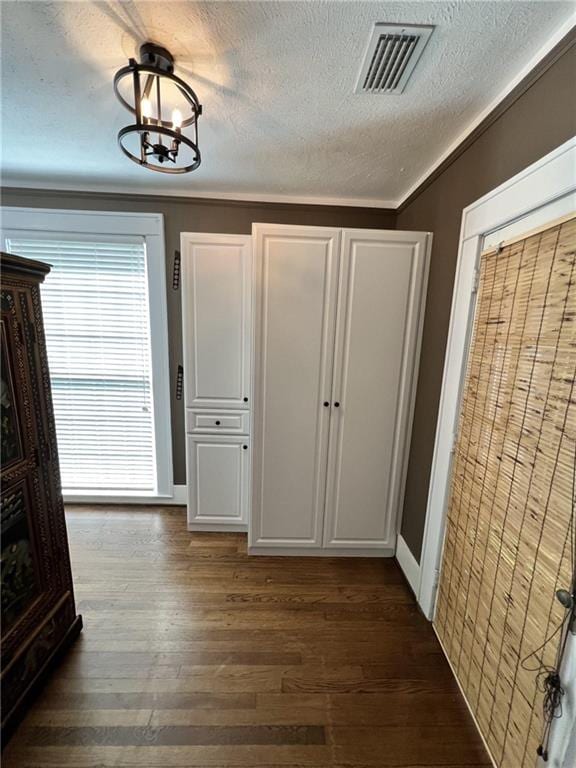 unfurnished bedroom featuring ornamental molding, dark wood-type flooring, a textured ceiling, and a notable chandelier