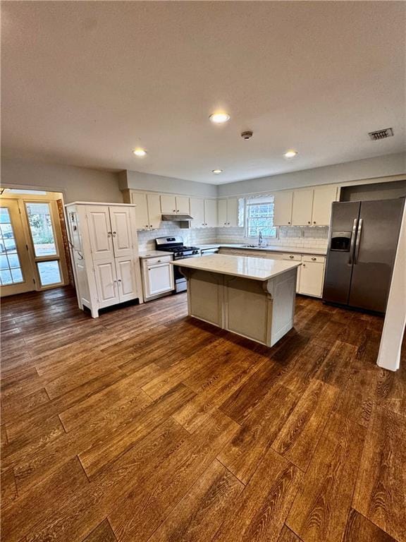 kitchen with white cabinetry, a center island, appliances with stainless steel finishes, dark hardwood / wood-style flooring, and backsplash