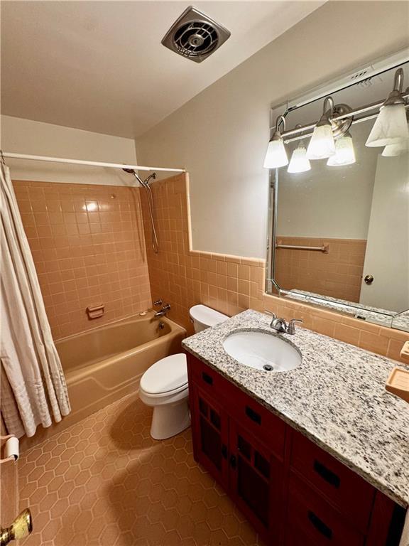 full bathroom featuring toilet, tile walls, vanity, shower / bathtub combination with curtain, and tile patterned flooring