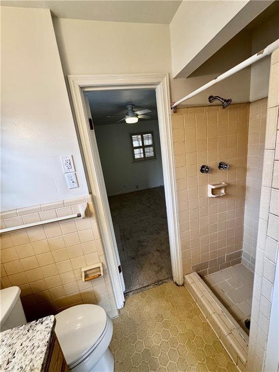 bathroom with tile walls, vanity, toilet, and a tile shower