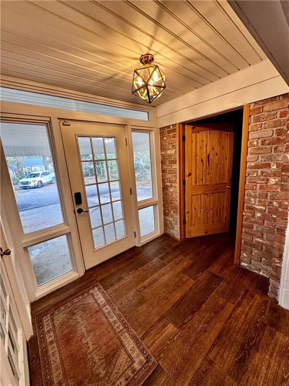 doorway featuring dark hardwood / wood-style flooring, wooden ceiling, and brick wall