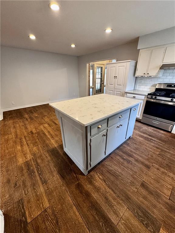 kitchen featuring dark wood-type flooring, backsplash, stainless steel gas range oven, light stone countertops, and a kitchen island