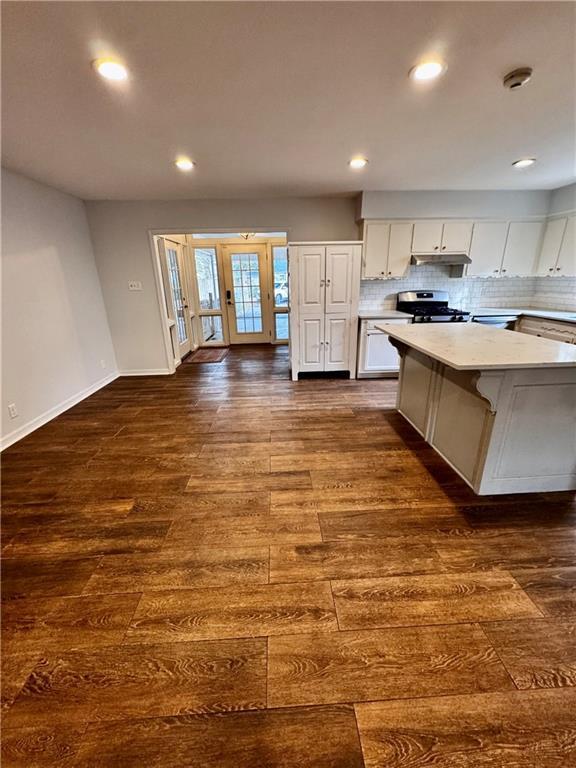 kitchen with a breakfast bar area, backsplash, stainless steel range, white cabinets, and dark hardwood / wood-style flooring