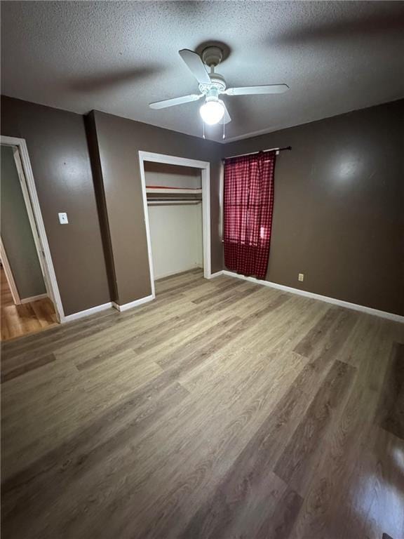 unfurnished bedroom featuring a textured ceiling, baseboards, and wood finished floors