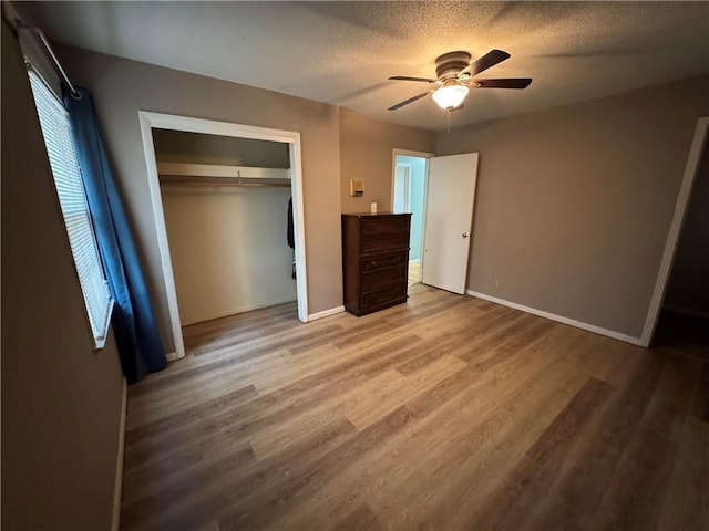 unfurnished bedroom featuring wood finished floors, baseboards, a closet, and a textured ceiling