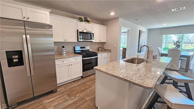 kitchen featuring appliances with stainless steel finishes, white cabinets, a center island with sink, and sink