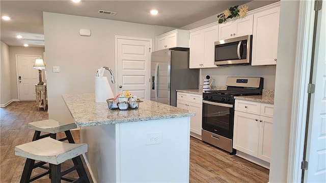 kitchen with light stone counters, stainless steel appliances, a kitchen island with sink, a breakfast bar area, and white cabinets