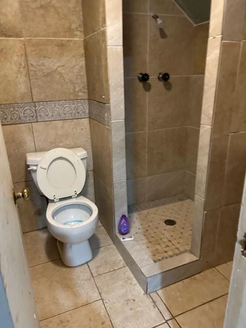 bathroom with tiled shower, toilet, tile patterned flooring, and tile walls