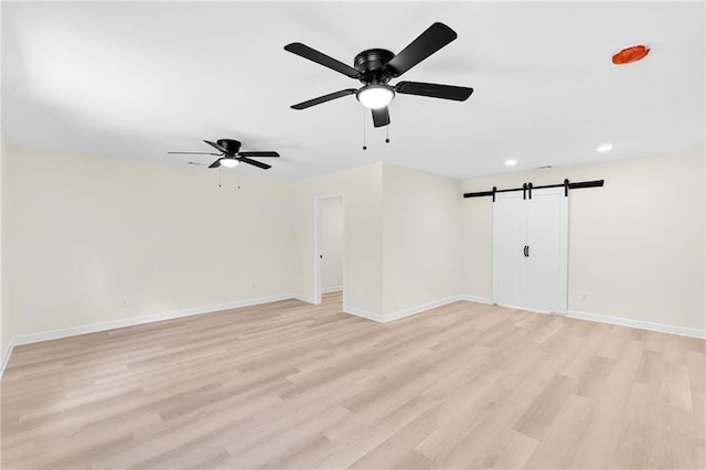 empty room featuring light hardwood / wood-style floors, a barn door, and ceiling fan