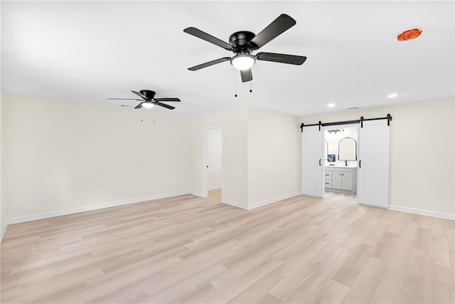 unfurnished living room featuring ceiling fan, a barn door, and light wood-type flooring