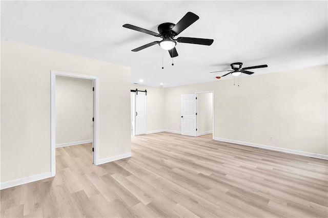 unfurnished room with a barn door, ceiling fan, and light hardwood / wood-style flooring