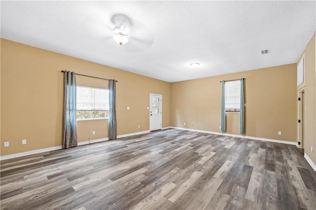 spare room with a textured ceiling, wood finished floors, visible vents, and baseboards