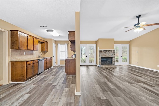 kitchen featuring a fireplace, visible vents, stainless steel dishwasher, brown cabinets, and tasteful backsplash