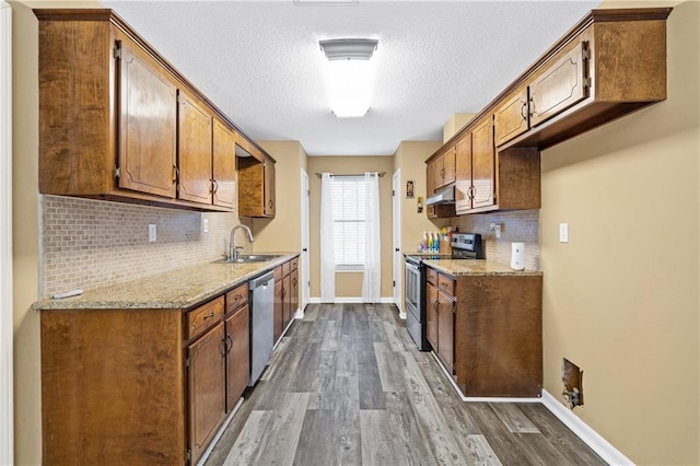 kitchen with under cabinet range hood, stainless steel appliances, dark wood-type flooring, a sink, and baseboards