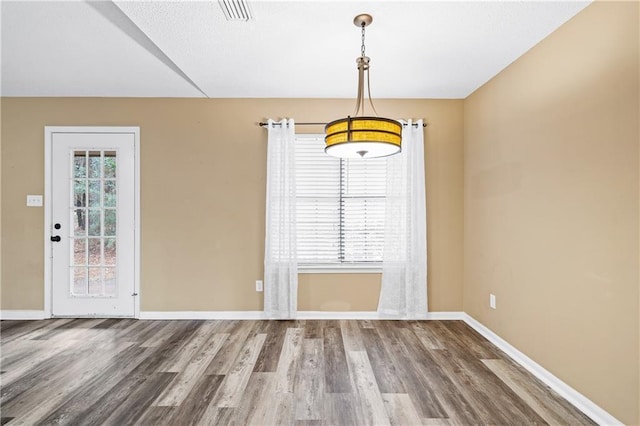 unfurnished dining area with visible vents, baseboards, and wood finished floors