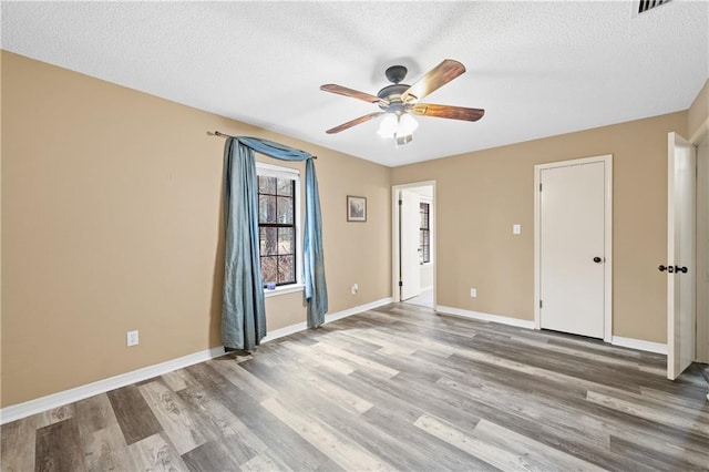 empty room with ceiling fan, a textured ceiling, baseboards, and wood finished floors