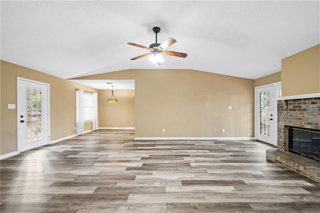 unfurnished living room featuring lofted ceiling, a brick fireplace, wood finished floors, and baseboards