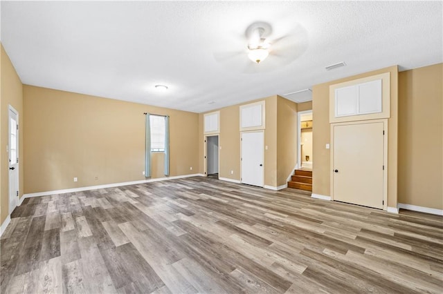 unfurnished living room with stairway, baseboards, visible vents, and wood finished floors