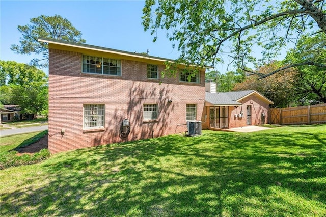 rear view of house with central air condition unit, a chimney, brick siding, fence, and a lawn