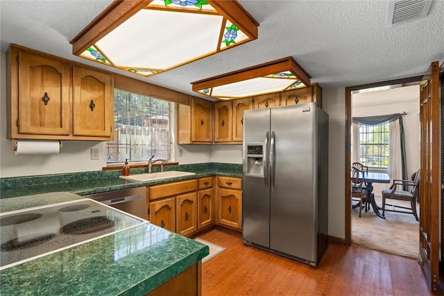 kitchen featuring brown cabinetry, appliances with stainless steel finishes, a sink, dark countertops, and light wood finished floors