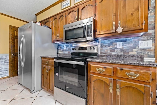 kitchen with light tile patterned floors, tasteful backsplash, crown molding, appliances with stainless steel finishes, and brown cabinetry