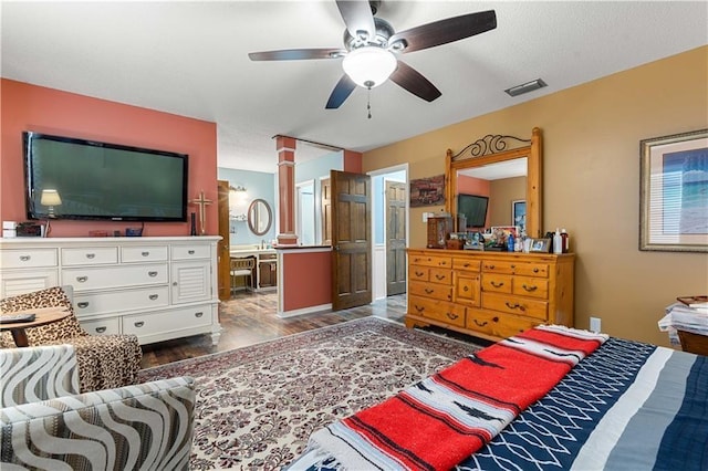 bedroom featuring wood finished floors, ensuite bath, decorative columns, ceiling fan, and visible vents