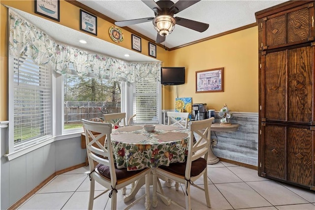 dining space featuring a ceiling fan, ornamental molding, a wainscoted wall, and light tile patterned flooring