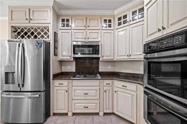 9791 Aspen Cir, Daphne, AL 36527 - kitchen with stainless steel appliances, cream cabinetry, dark stone countertops, light tile patterned floors, and crown molding
