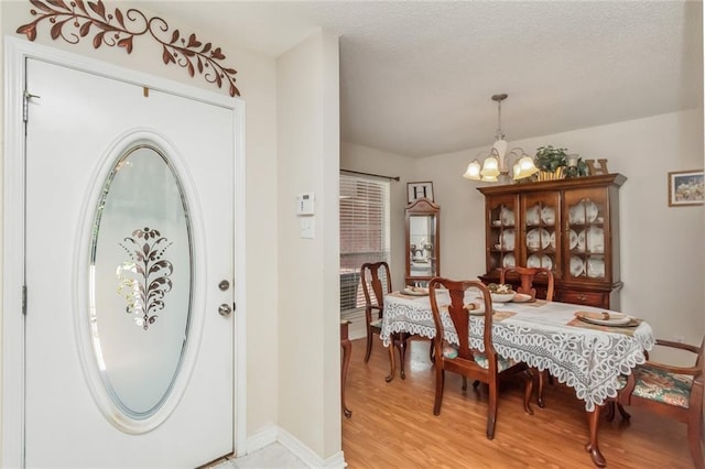 dining space with a textured ceiling, a notable chandelier, and light wood-type flooring