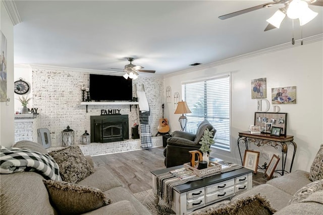 living room with ceiling fan, hardwood / wood-style flooring, crown molding, and a brick fireplace