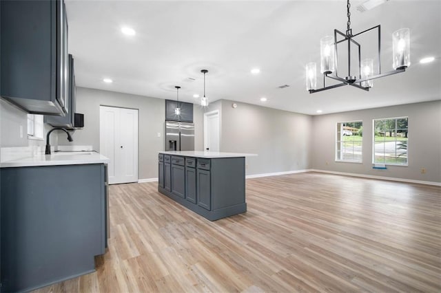 kitchen with a sink, light countertops, light wood-style floors, stainless steel refrigerator with ice dispenser, and a chandelier