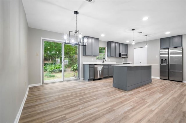 kitchen featuring light wood finished floors, gray cabinetry, light countertops, a notable chandelier, and stainless steel appliances