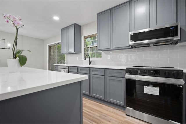 kitchen with stainless steel microwave, light wood-type flooring, gray cabinets, and range with electric stovetop