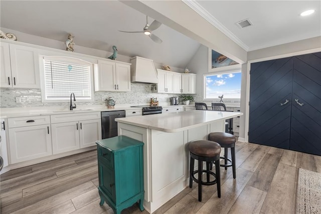 kitchen with custom range hood, white cabinetry, a kitchen island, dishwasher, and light wood-type flooring