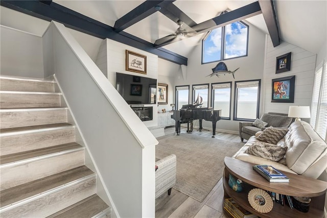 living room with ceiling fan, beamed ceiling, light wood-type flooring, and high vaulted ceiling