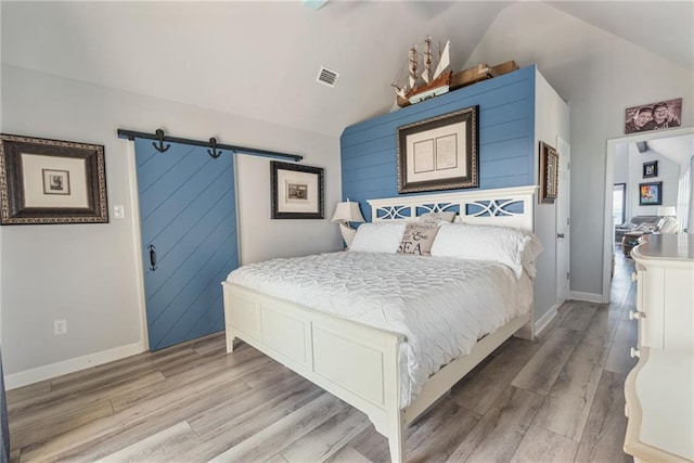 bedroom featuring a barn door, light hardwood / wood-style floors, and vaulted ceiling