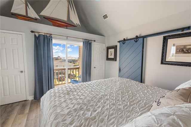 bedroom featuring vaulted ceiling, hardwood / wood-style flooring, access to exterior, and a barn door