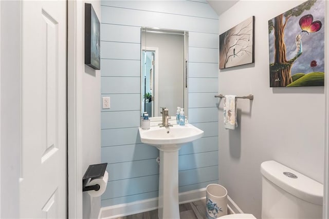 bathroom featuring wood walls, hardwood / wood-style floors, and toilet