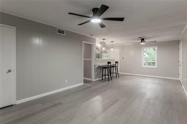 unfurnished living room featuring hardwood / wood-style flooring, ceiling fan, ornamental molding, and a textured ceiling