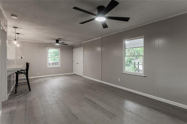 unfurnished living room with ceiling fan with notable chandelier, dark hardwood / wood-style flooring, ornamental molding, and a textured ceiling