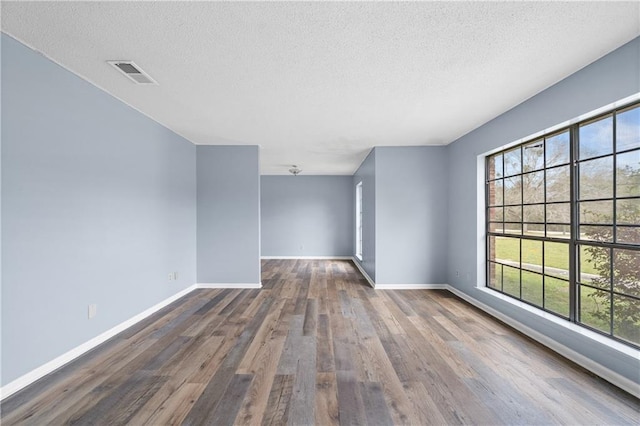 spare room featuring a textured ceiling, wood finished floors, visible vents, and baseboards