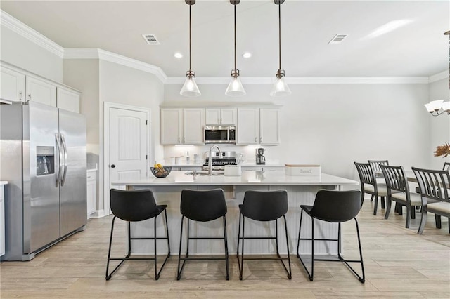 kitchen with white cabinetry, appliances with stainless steel finishes, decorative light fixtures, and a kitchen island with sink