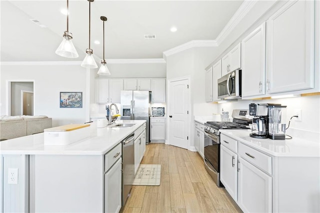 kitchen with appliances with stainless steel finishes, an island with sink, white cabinets, hanging light fixtures, and crown molding