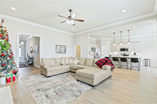 living room featuring ceiling fan, ornamental molding, sink, and light hardwood / wood-style flooring