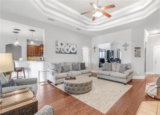 living room featuring dark hardwood / wood-style floors, ceiling fan, a tray ceiling, and crown molding